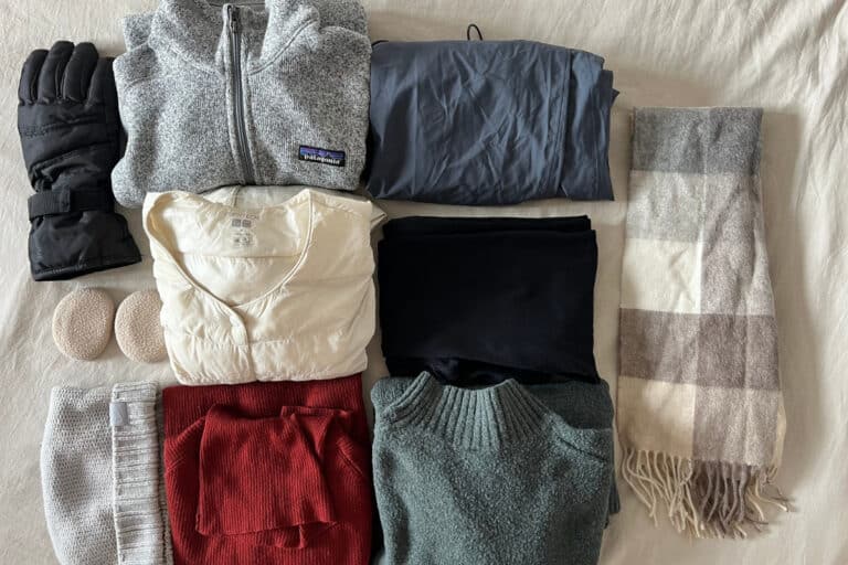 A full winter clothing layout featuring gloves, a fleece zip-up, waterproof pants, a puffer vest, thermal layers, sweaters, a scarf, and ear warmers. This complete set shows exactly what to wear in Hokkaido winter to stay warm.